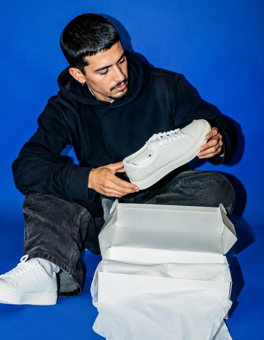 A creator unboxing white sneakers against a cobalt backdrop